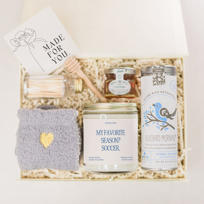 a gift box containing a candle, a jar of honey, a cup of tea