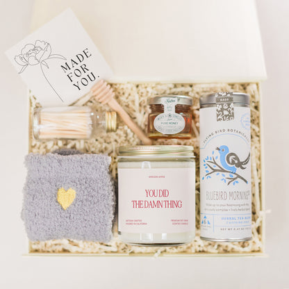 a gift box containing a candle, a jar of honey, a card and a